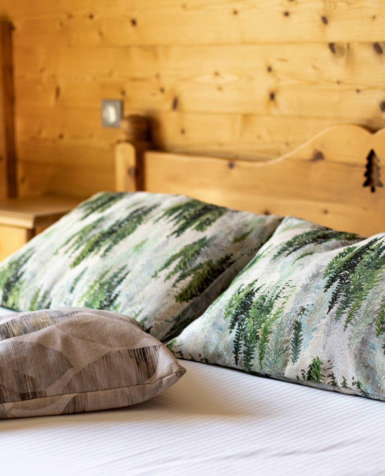 Détail de coussins à motif sapins sur un lit en bois, déco montagne de l'hôtel La Réserve Gérardmer