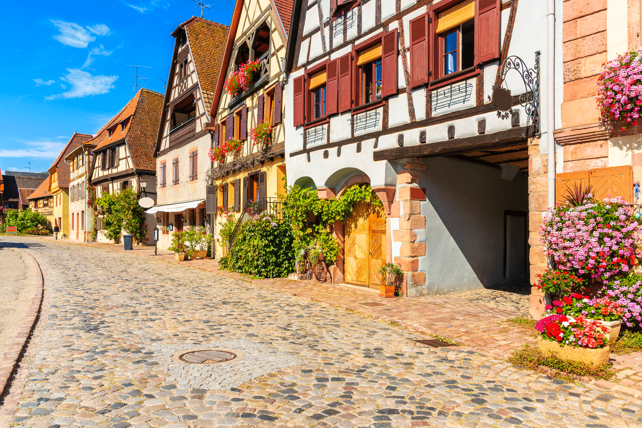 Rue pavée et maisons à colombages fleuries d'un village de la route des vins d'Alsace