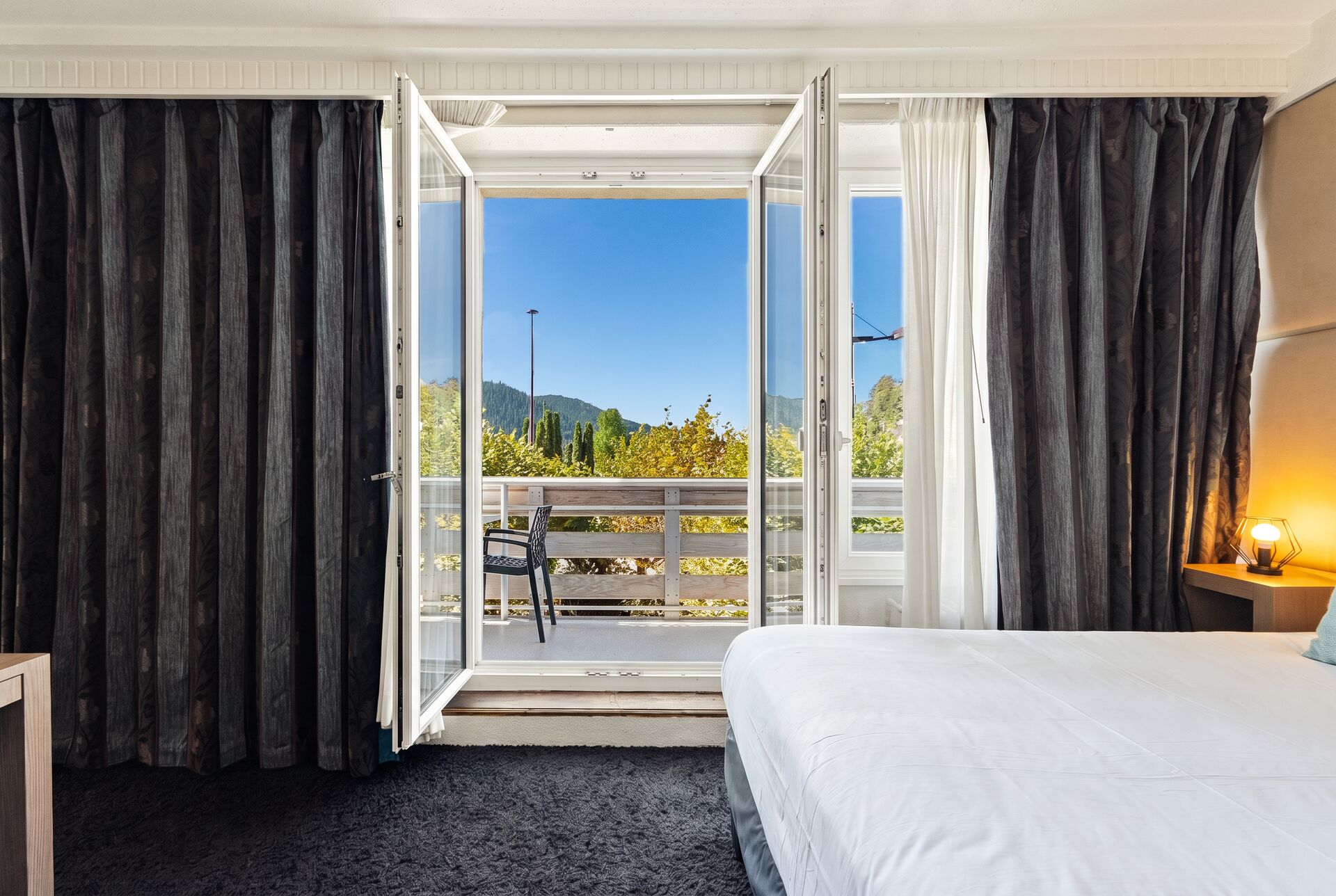 Porte-fenêtre ouverte sur le balcon et le lac, chambre deluxe de l'hôtel La Réserve Gérardmer